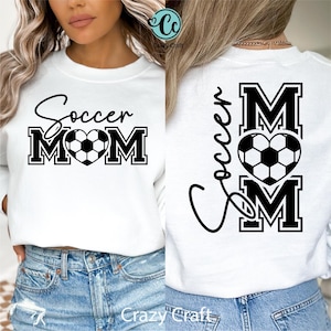 May include: White sweatshirt with the text "Soccer Mom" in black script and block letters, featuring a soccer ball heart design. The back of the sweatshirt also displays the text "Soccer Mom" with a soccer ball heart.