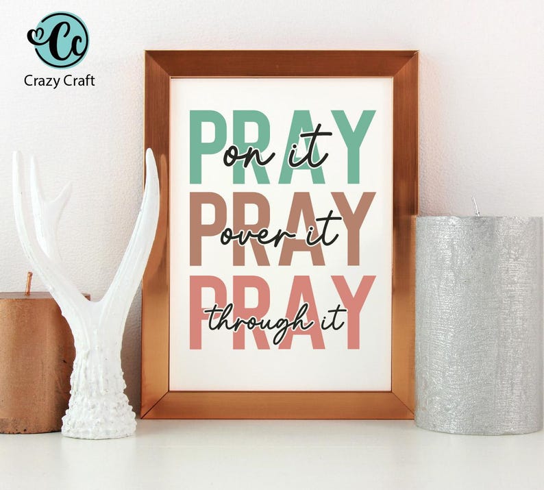 K&ouml;nnte beinhalten: Gerahmter Druck mit den Worten "PRAY on it, over it, through it" in T&uuml;rkis, Braun und Rosa. Eine wei&szlig;e dekorative Geweih und eine silberne Kerze befinden sich an den Seiten. Das Crazy Craft-Logo befindet sich oben links.