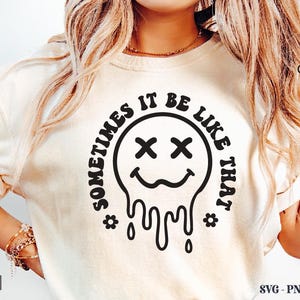 Pu&ograve; includere: T-shirt color crema con grafica nera di una faccina sorridente che si scioglie e la scritta "SOMETIMES IT BE LIKE THAT" in un design circolare. La maglietta ha anche la parola "Digital" in basso a sinistra e "Crazy Craft" in alto a destra.