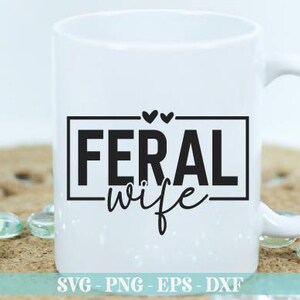 May include: White ceramic mug with a black graphic that says "Feral Wife" in a rectangular frame with two small hearts above the text.