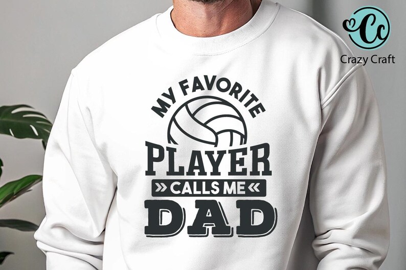 K&ouml;nnte beinhalten: Wei&szlig;es Sweatshirt mit einem schwarzen Aufdruck, der "MY FAVORITE PLAYER CALLS ME DAD" mit einem Volleyball-Bild zeigt. Das Crazy Craft-Logo befindet sich in der oberen rechten Ecke.