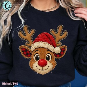 Puede incluir: Una sudadera negra de cuello redondo con un gráfico central de una cara de reno con grandes astas marrones, un gorro de Papá Noel rojo con borde beige, orejas con estampado de cuadros rojos y negros y una nariz roja.