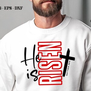 May include: White sweatshirt with the text "He is Risen" in black and red, with a black cross. The text "Matthew 28:6" is below the cross. The Crazy Craft logo is in the upper right corner.