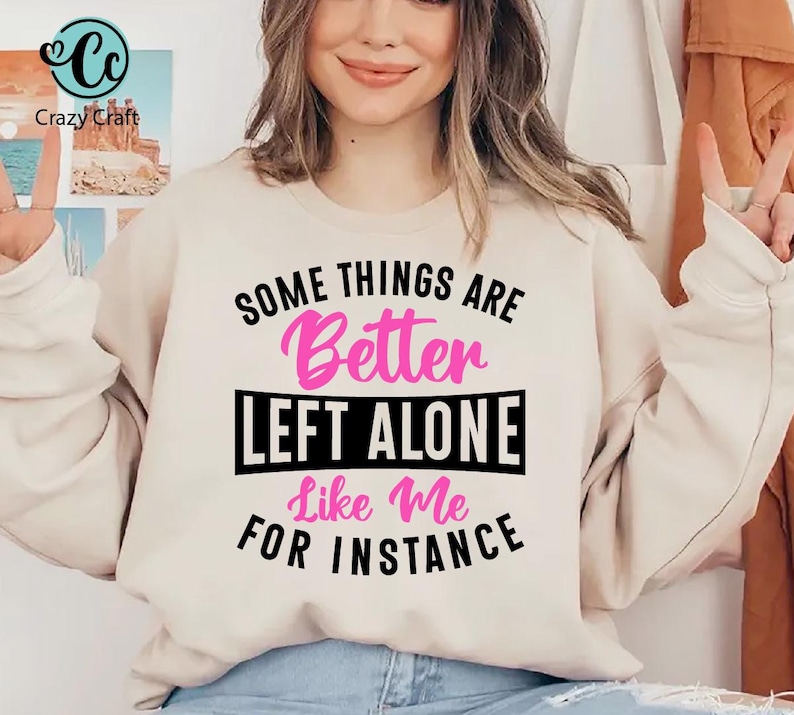 May include: A beige sweatshirt with the text "SOME THINGS ARE Better LEFT ALONE Like Me FOR INSTANCE" in black and pink. The sweatshirt is being worn by a person. The Crazy Craft logo is in the upper left corner.