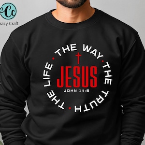 May include: Black crewneck sweatshirt with the text "JESUS" in red, encircled by "THE WAY, THE TRUTH, THE LIFE" in white. A red cross is above "JESUS". The text "John 14:6" is below. The Crazy Craft logo is in the upper left.