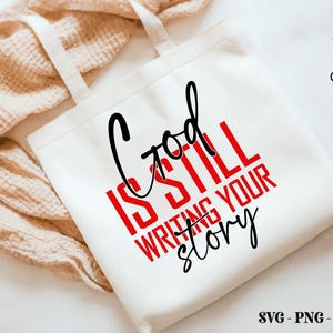 May include: White tote bag with black handles and the text "God is still writing your story" in red and black lettering.