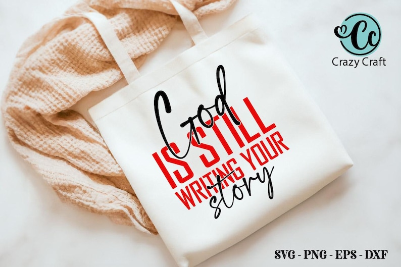 May include: White tote bag with black handles and the text "God is still writing your story" in red and black lettering.