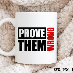 以下が含まれることがあります： 黒と赤で「PROVE THEM WRONG」の文字が入った白いセラミックマグ。マグには大きなハンドルが付いており、柔らかい質感の背景に置かれています。マグはコーヒーや紅茶の標準サイズです。