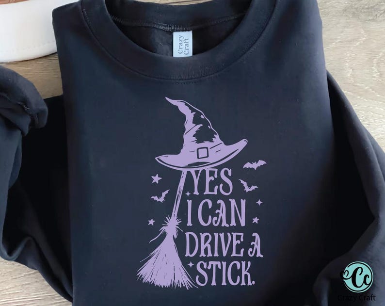 K&ouml;nnte beinhalten: Schwarzes Sweatshirt mit lila Hexenhut, Besen, Flederm&auml;usen und Sternen. Der Text lautet: "YES I CAN DRIVE A STICK."