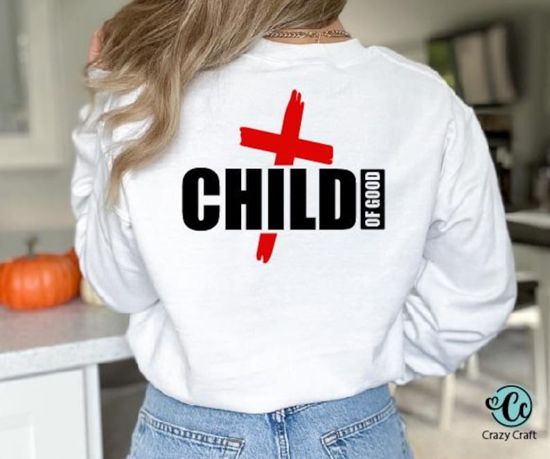 以下が含まれることがあります： 黒い文字で「CHILD OF GOOD」と赤い十字のデザインが施された白いスウェットシャツ。クルーネックと長袖です。Crazy Craftのロゴが右下に表示されています。