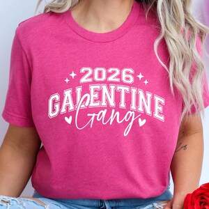 May include: A magenta t-shirt with the text "2026 Galentine Gang" in white, with star and heart accents. The shirt is a crew neck style and is made of a soft material. The shirt is a Valentine's Day themed item.