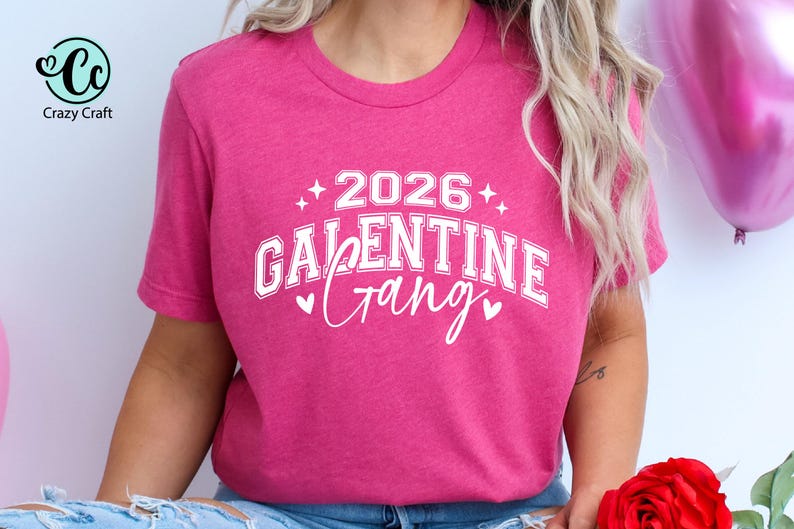 May include: A magenta t-shirt with the text "2026 Galentine Gang" in white, with star and heart accents. The shirt is a crew neck style and is made of a soft material. The shirt is a Valentine's Day themed item.