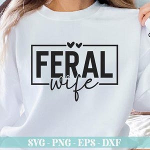May include: White sweatshirt with black text that reads "FERAL wife" in a box with two hearts above the text.