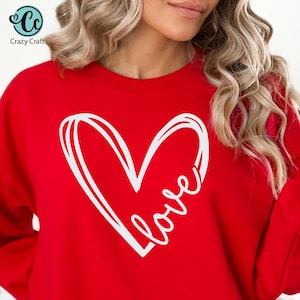 Puede incluir: Sudadera roja con un contorno blanco de un corazón y la palabra "love" dentro del corazón.