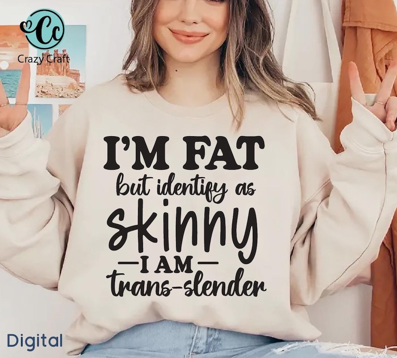 Pu&ograve; includere: Una felpa beige con la scritta "I'M FAT but identify as skinny - I AM - trans-slender" in nero. La felpa &egrave; indossata da una persona. La parola "Digital" si trova nell'angolo in basso a sinistra.