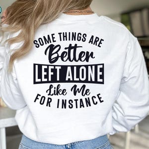 May include: White sweatshirt with the text "SOME THINGS ARE Better LEFT ALONE Like Me FOR INSTANCE" in black. The Crazy Craft logo is in the upper left corner. The sweatshirt is being worn.