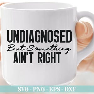 May include: White ceramic coffee mug with black text that reads "UNDIAGNOSED But Something AIN'T RIGHT".