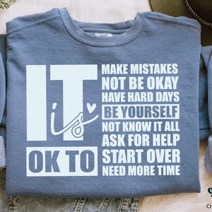 May include: A blue sweatshirt with white text that reads "It is OK to make mistakes, not be okay, have hard days, be yourself, not know it all, ask for help, start over, need more time".