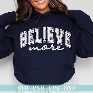 May include: Navy blue hoodie with the words "BELIEVE more" in white block letters. The word "BELIEVE" is arched across the chest, and "more" is written in a cursive font below. The hoodie has a front pocket and a drawstring hood.