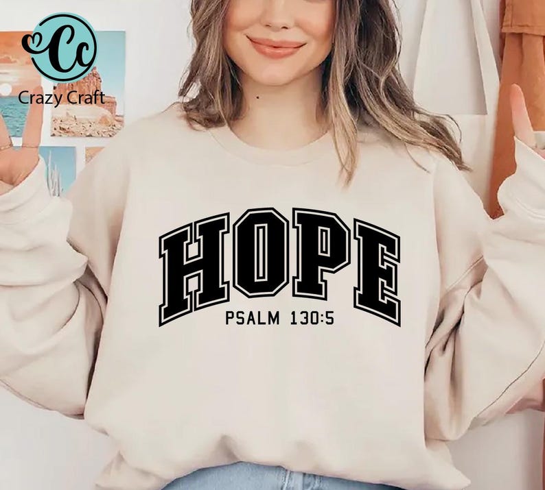 K&ouml;nnte beinhalten: Ein cremefarbener Pullover mit dem Wort "HOPE" in schwarzen Blockbuchstaben mit schwarzem Umriss. Der Text "PSALM 130:5" ist in Schwarz unter dem Wort "HOPE" gedruckt.