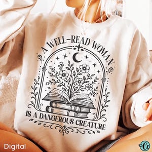 May include: A beige crewneck sweatshirt featuring a black graphic print of a stack of books with flowers blooming from the top book, enclosed in an arched frame with stars and a crescent moon, and the text A WELL-READ WOMAN IS A DANGEROUS CREATURE.