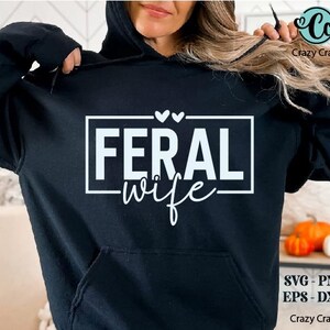 May include: A black hoodie with a white graphic that says "Feral wife" in a rectangle with two small hearts above it.