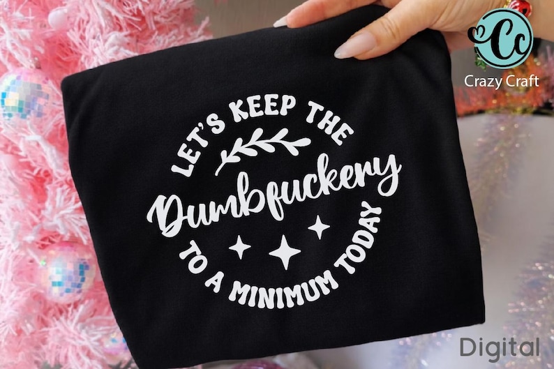Pu&ograve; includere: T-shirt nero con la scritta bianca "LET'S KEEP THE Dumbfuckery TO A MINIMUM TODAY" in un design circolare. Il design include un rametto e quattro stelle. Il logo Crazy Craft si trova nell'angolo in alto a destra.