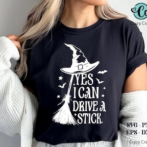 K&ouml;nnte beinhalten: Schwarzes T-Shirt mit wei&szlig;er Grafik, die einen Hexenhut, einen Besen, Flederm&auml;use und Sterne zeigt. Der Text lautet "YES I CAN DRIVE A STICK." Das Design umfasst SVG-, PNG-, EPS- und DXF-Dateiformate.