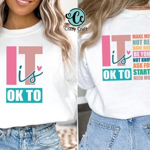 May include: White sweatshirt with the text "It is OK to" on the front and a list of phrases on the back, including "Make Mistakes", "Not Be Okay", "Have Hard Days", "Be Yourself", "Not Know It All", "Ask For Help", "Start Over", and "Need More Time".