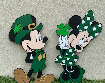 Puede incluir: Mickey Mouse y Minnie Mouse vestidos con atuendos de San Patricio en verde y blanco. Mickey lleva un sombrero verde con un trébol y un chaleco verde. Minnie lleva un vestido verde con lunares blancos y un lazo verde.