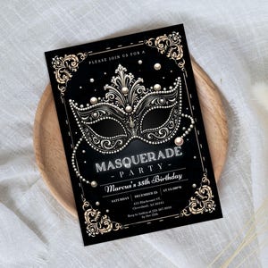 May include: A black rectangular invitation card featuring a central ornate masquerade mask graphic in gold and white. The text reads: PLEASE JOIN US FOR A MASQUERADE PARTY, Marcus's 35th Birthday, SATURDAY, DECEMBER 25, AT 10:30PM, 455 Blackcrest ST, Clevelend, AD 56345.