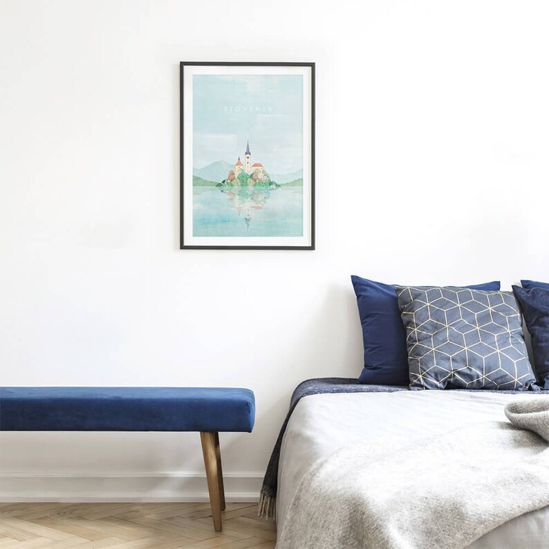 K&ouml;nnte beinhalten: Ein Aquarellbild einer Kirche auf einer Insel in einem See. Das Bild ist in Schwarz gerahmt und h&auml;ngt an einer wei&szlig;en Wand &uuml;ber einer blauen Samtbank und einem Bett mit blauen und grauen Kissen.