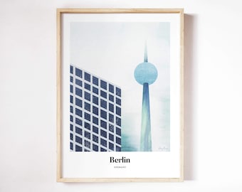 May include: A framed print of a stylized illustration of the Berlin skyline. The print features a blue and white building and a tall tower with a blue sphere on top. The text "Berlin, Germany" is printed at the bottom of the print.