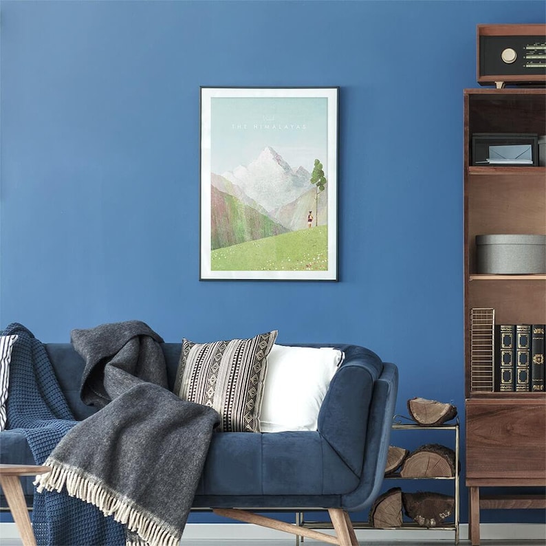 May include: A framed print of a mountain landscape with the text "The Himalayas" at the top. The print features a green field with a single tree and a small figure in the distance.
