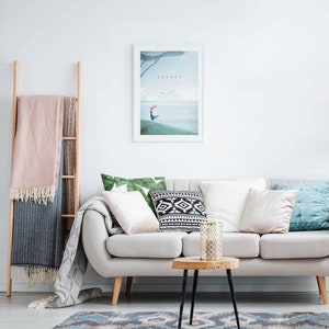 May include: A living room scene with a light gray sofa, pillows, and a wooden side table. A framed print with the word "SYDNEY" hangs on the wall. A wooden ladder holds blankets, and a patterned rug is on the floor.