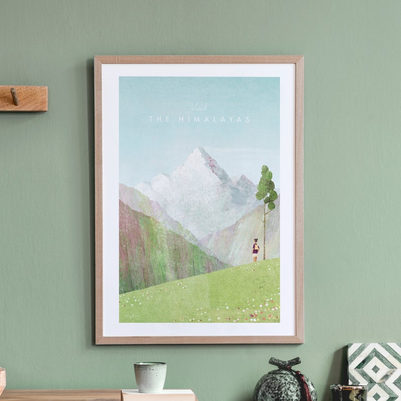 May include: A framed poster featuring a watercolour illustration of a mountain range with a person standing in the foreground. The text 'Visit The Himalayas' is at the top of the poster.