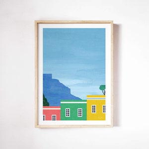 Peut inclure: Une illustration encadrée de maisons colorées avec une montagne en arrière-plan. Les maisons sont jaunes, vertes et rouges avec des fenêtres blanches. La montagne est bleue et le ciel est bleu clair.