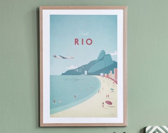 May include: A framed poster with a retro travel illustration of Rio de Janeiro, Brazil. The poster features a blue sky, a green mountain, a beach with people, and a plane flying overhead. The text "Visit RIO" is in red letters.