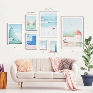 May include: A collection of framed art prints, including scenes of Peru, Cornwall, New York, and Florence. The prints vary in size, with the largest measuring 50cm x 70cm. The artwork features minimalist designs in pastel colors, displayed above a cream-colored sofa.