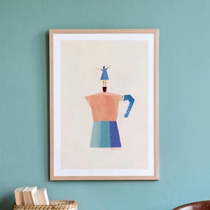 Op de afbeelding: Een ingelijste kunstdruk met een gestileerde illustratie van een persoon in een blauwe jurk die op een roze en blauwe mokkapot staat. De mokkapot heeft een blauw handvat en een kleine donkerbruine voet op een lichte crèmekleurige achtergrond.