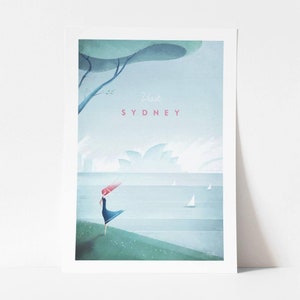 May include: A framed art print featuring a stylized illustration of Sydney, Australia. The artwork depicts a person standing near the water with the Sydney Opera House in the background. The text "Visit SYDNEY" is displayed in pink.