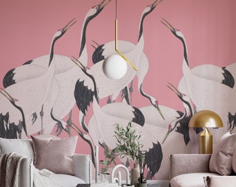 May include: A living room interior with a pink wall featuring a wallpaper pattern of white cranes with black accents. The room is decorated with a white globe pendant light, a black marble coffee table, a white throw blanket, a pink sofa, and a pink armchair.
