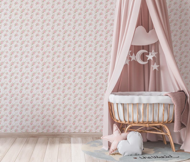 May include: A pink floral wallpaper with a white wicker bassinet with a white canopy and a white cloud mobile hanging above it. The bassinet is decorated with two pillows, one white and one pink star-shaped.