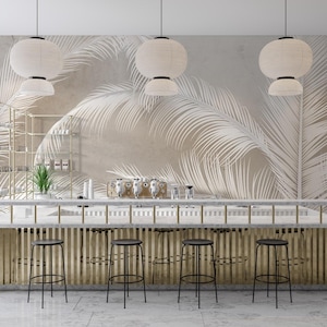 May include: A modern bar counter with a white marble top and a gold metal frame. The counter has a white and beige palm leaf patterned wallpaper behind it. There are four black metal bar stools in front of the counter.