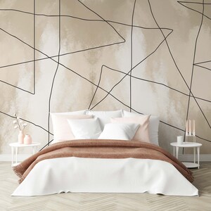 May include: A white bed with a brown blanket and pink pillows in front of a beige wall with black lines forming geometric shapes.