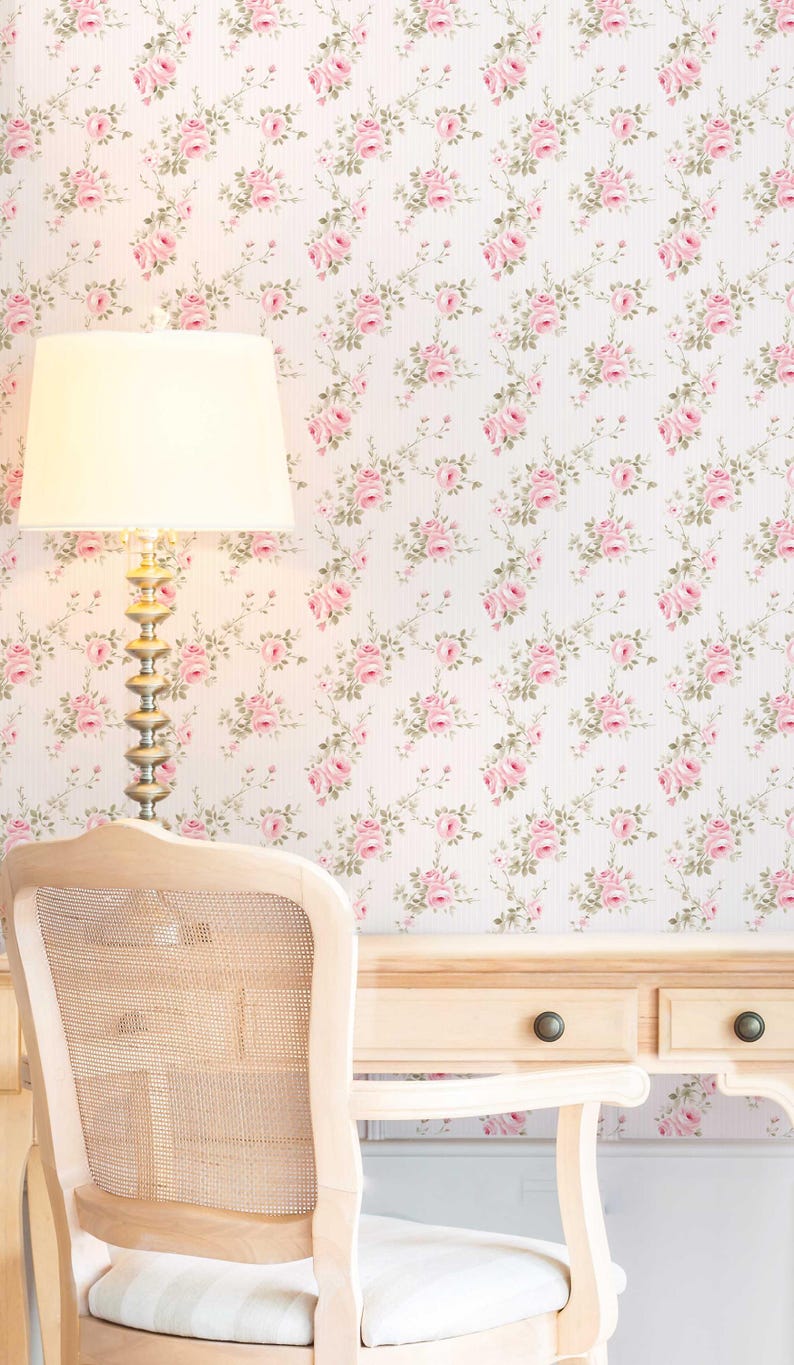 May include: A white desk with two drawers and a light wood chair with a woven back. The wall behind the desk is covered in pink floral wallpaper.