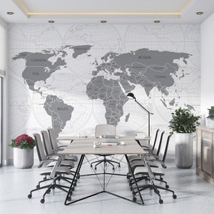 May include: A modern office space featuring a large world map mural in shades of gray. A long wooden table with multiple chairs is set up for meetings. The room is decorated with potted plants and a wooden cabinet, creating a professional atmosphere.