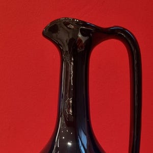 Peut inclure: Un pichet en céramique bleu foncé avec un glaçage blanc. Le pichet a un corps rond et un long col fin avec une anse.