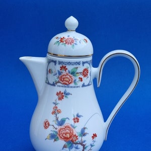 Peut inclure: Théière en porcelaine blanche avec un motif floral dans les tons de rouge, bleu et vert. La théière a un couvercle avec une bordure dorée et une poignée.