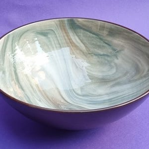 May include: A decorative bowl with a swirling pattern in shades of green, grey, and brown. The bowl has a dark brown rim and a deep purple exterior. The interior design resembles marble.